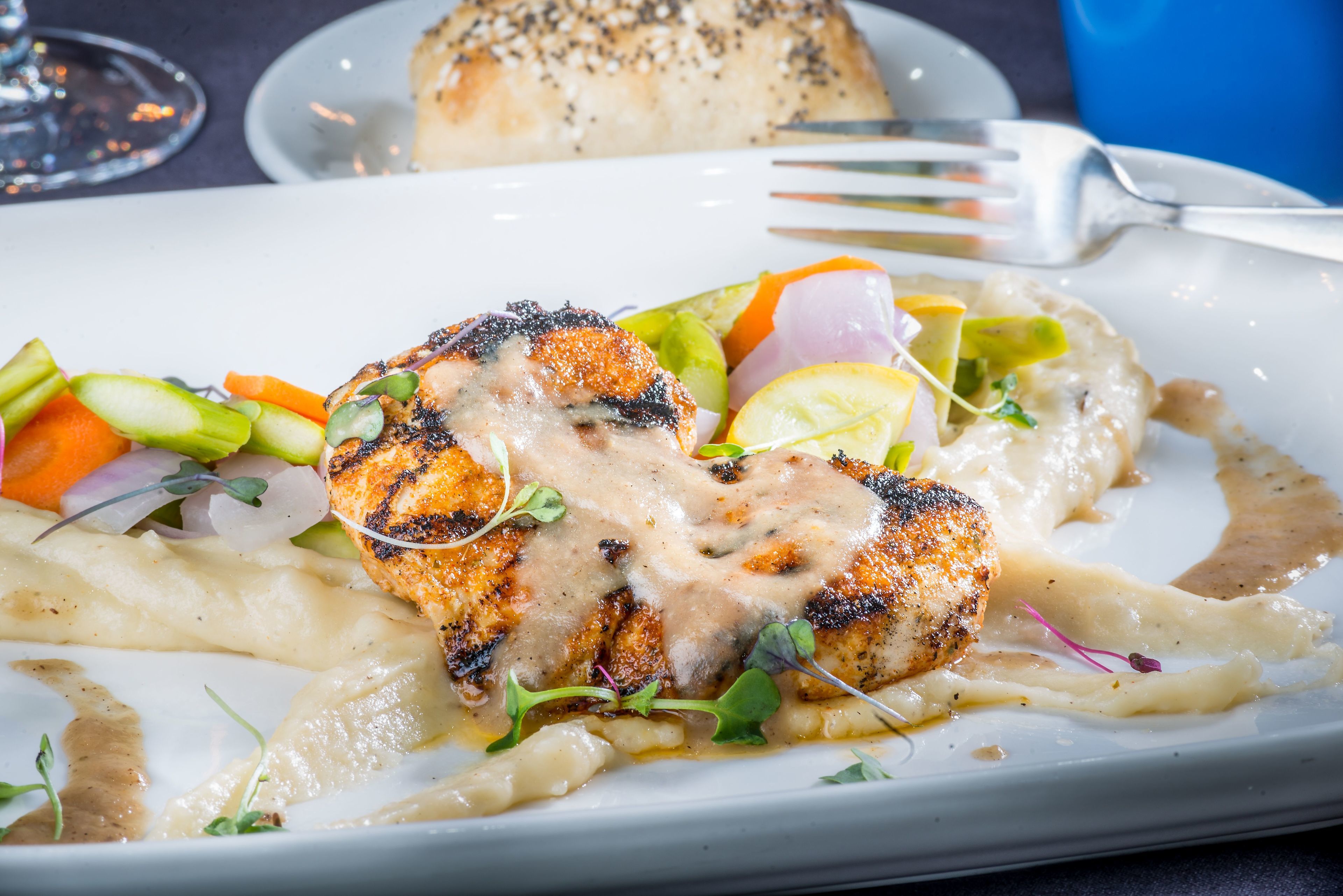 A plate of food with grilled fish, vegetables, and sauce.