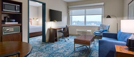 A hotel room with a bed, desk, chair, sofa, and a large window.