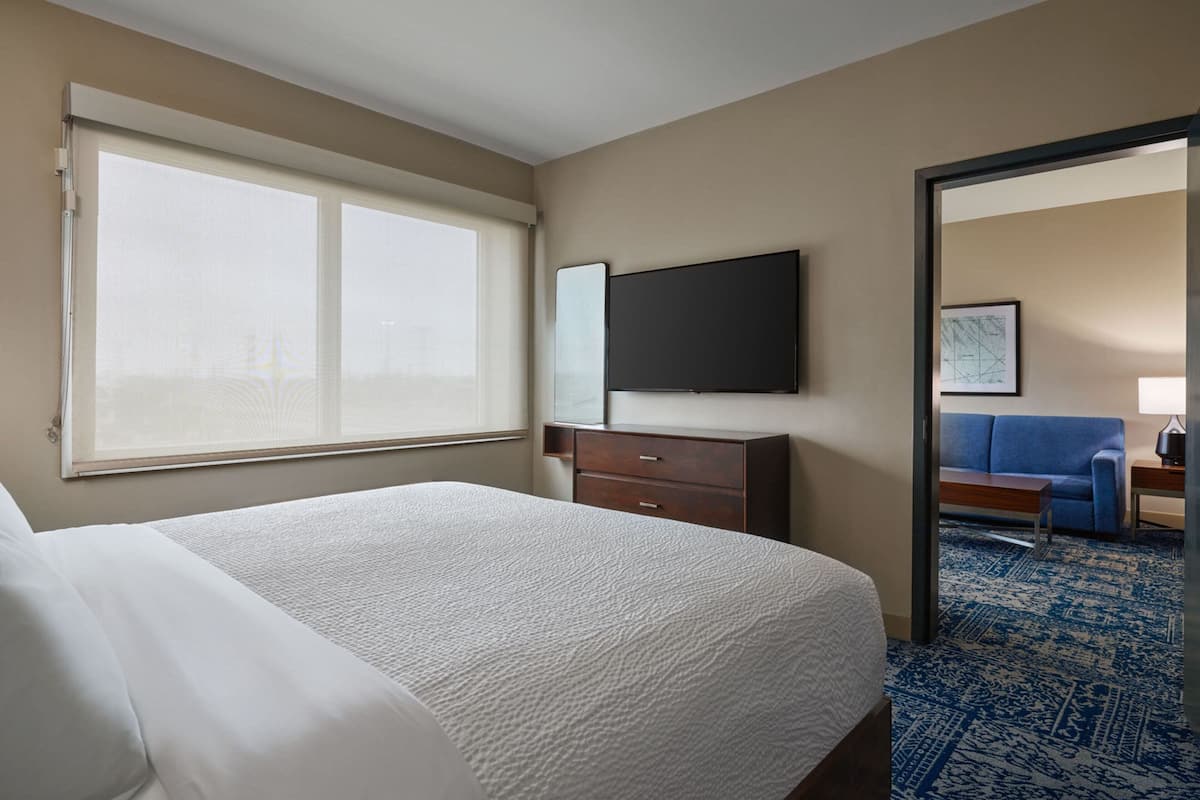 Een hotelkamer met een groot bed, een flatscreen televisie aan de muur, een houten nachtkastje, een blauwe bank en een kamerbreed tapijt met een patroon.
