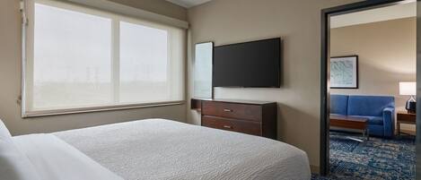 Ein Hotelzimmer mit einem großen Bett, einem Flachbildfernseher, einem Schminktisch und Blick auf die Stadt durch das Fenster.