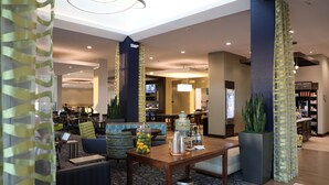 A hotel lobby with a wooden reception desk, seating area, and a large plant. - Hilton Garden Inn Austin Airport (Austin)