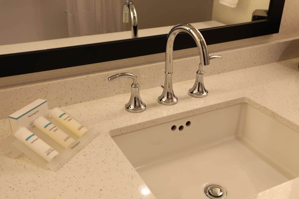 A bathroom sink with a mirror above it, a faucet, and three bottles of hand soap on the counter.