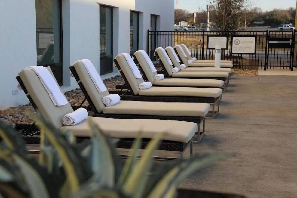 A row of sun loungers with towels, a paved walkway, and a fence with a sign.