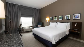 Una habitación de hotel con una cama grande, un escritorio, una silla, un televisor y una ventana con cortinas.