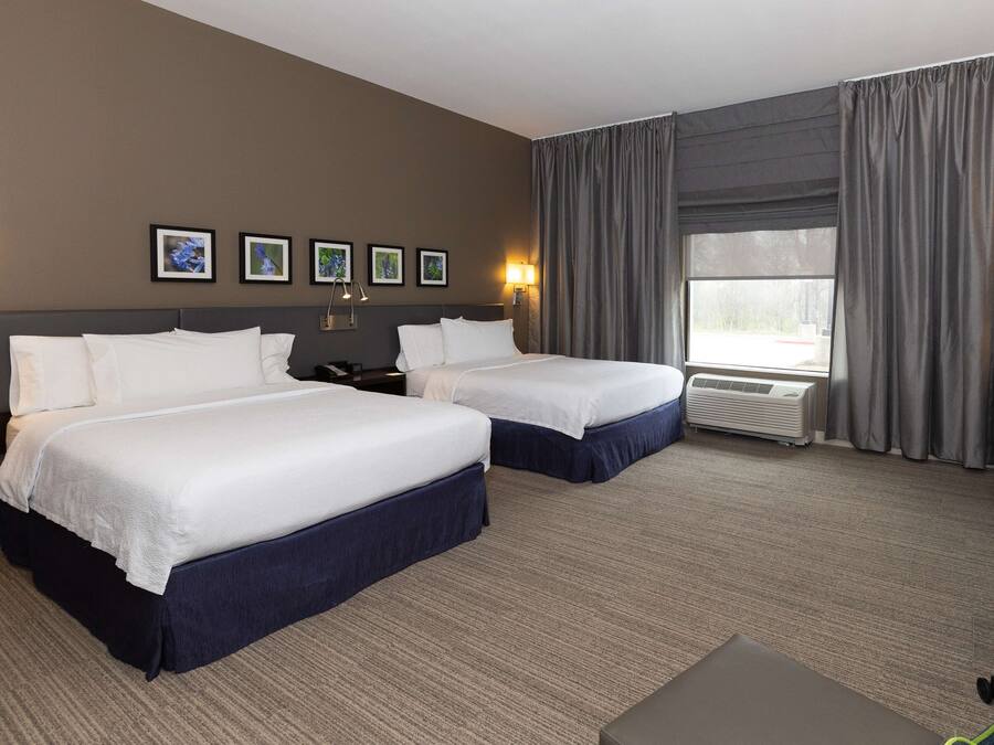 A hotel room with two beds, a desk, a chair, and a large window with curtains.