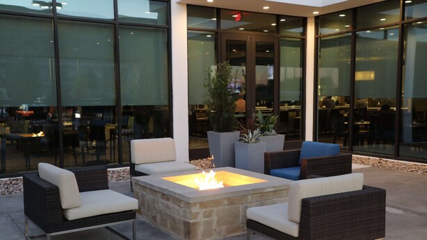 An outdoor seating area with wicker furniture and a central fire feature. - Hilton Garden Inn Austin Airport (Austin)