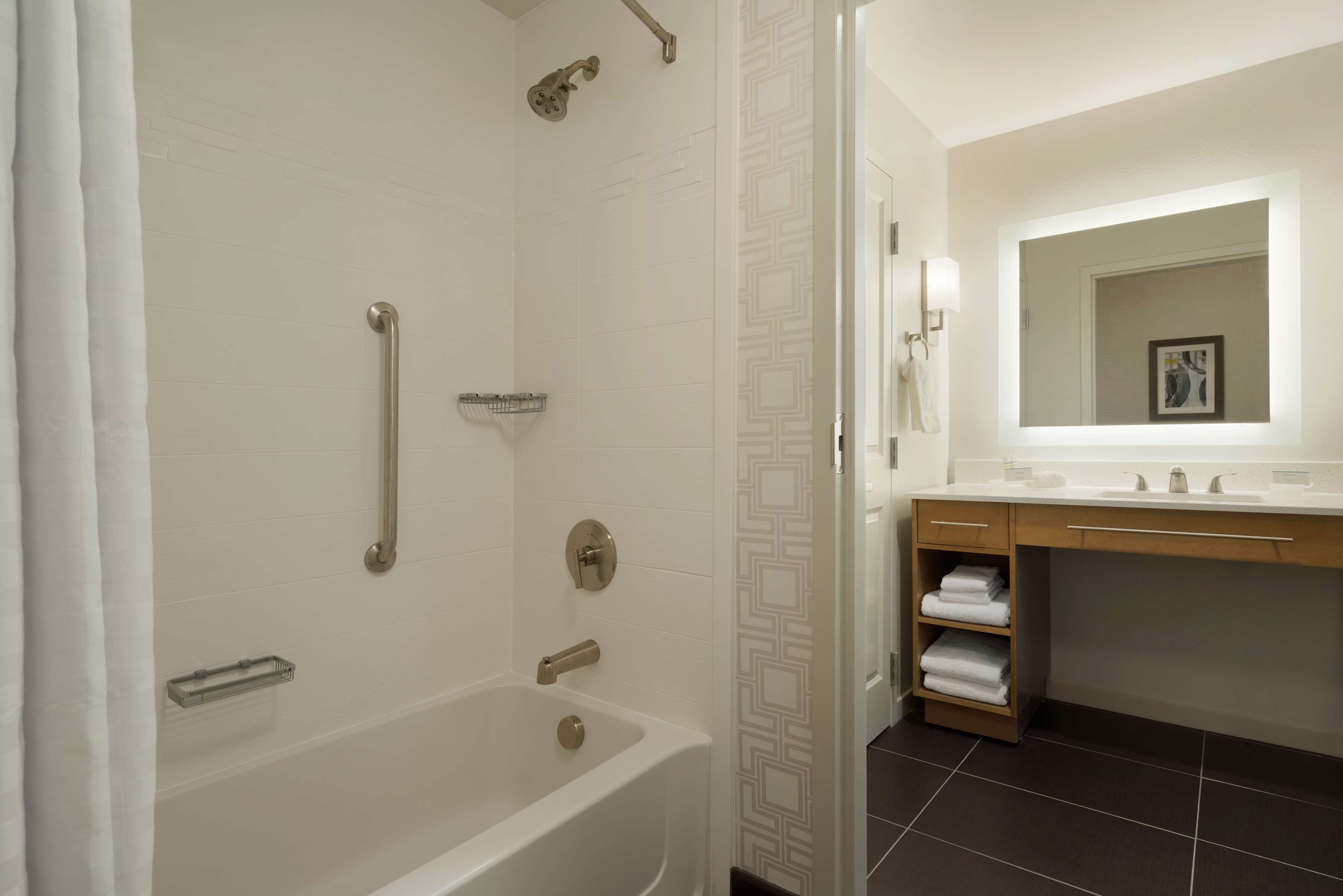 A modern bathroom with a bathtub, a shower with a handheld showerhead, a towel rack, and a vanity with a mirror and sink.