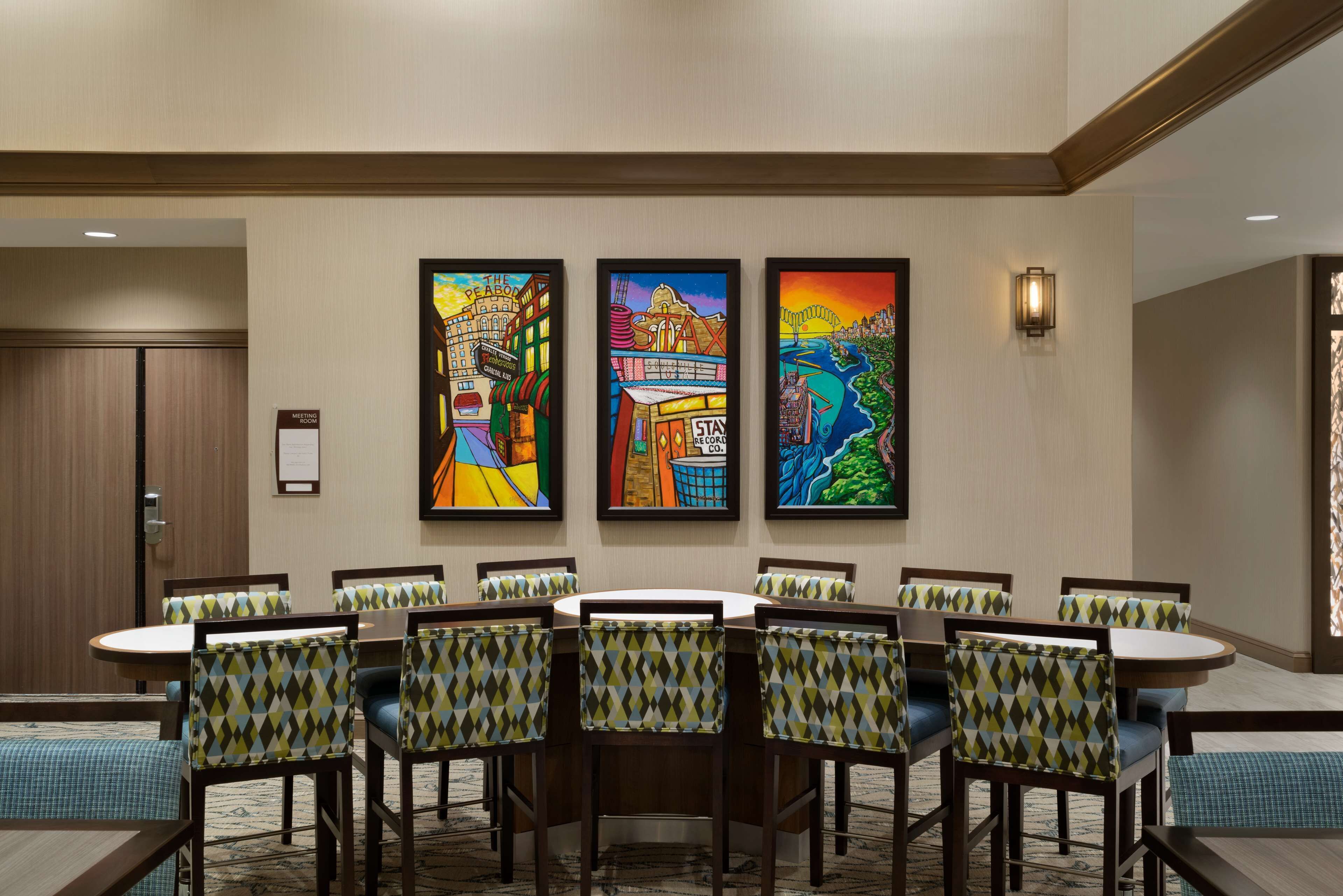 A conference room with a round table and chairs, framed artwork on the wall, and a sign indicating a meeting room.