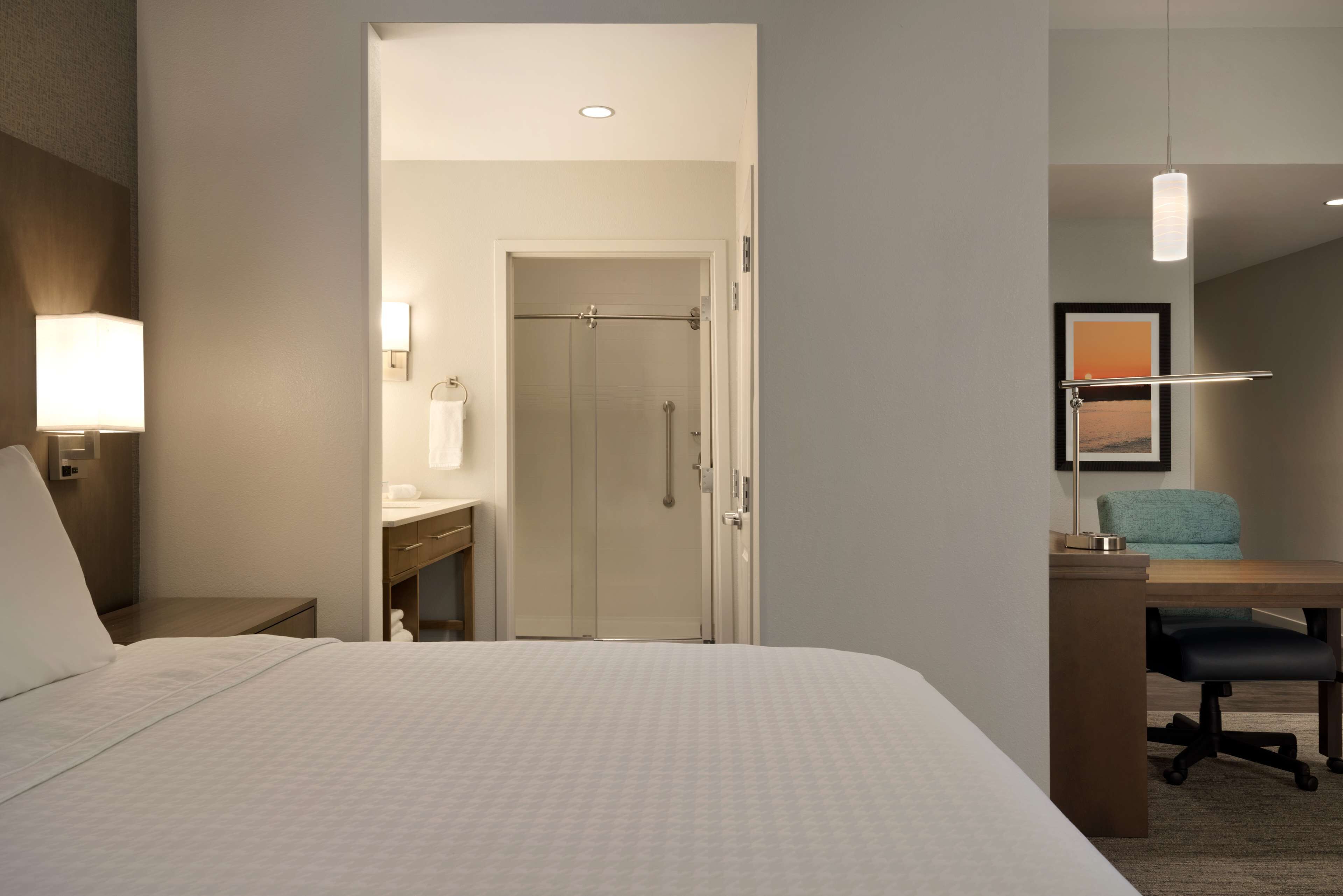 Camera d'albergo con un letto, una scrivania, una sedia, un bagno con doccia e un quadro appeso al muro.