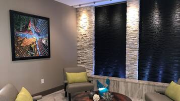 A modern living room with a large painting, two stone accent walls, and a round coffee table with decorative items.
