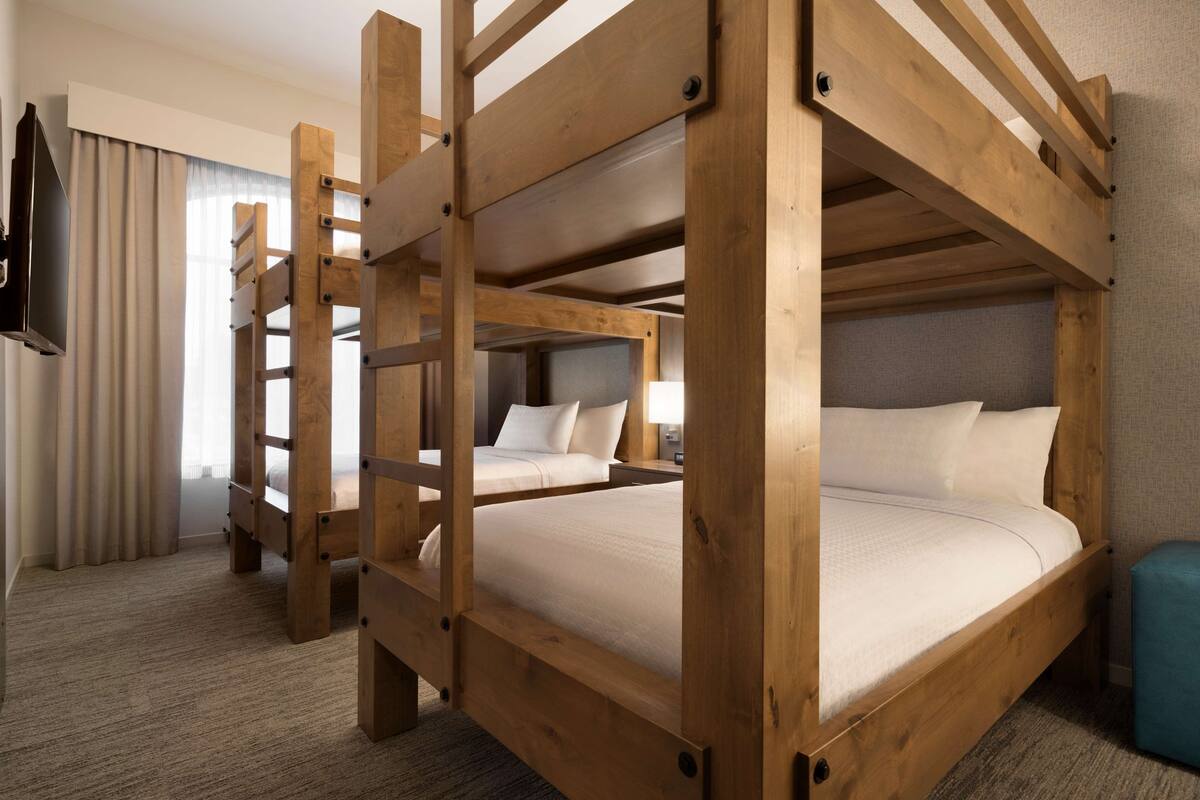 Een slaapkamer met stapelbed, een televisie aan de linkerkant en een raam met gordijnen.