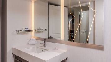 A modern bathroom with a white sink, a mirror, and a glass shelf above the sink.