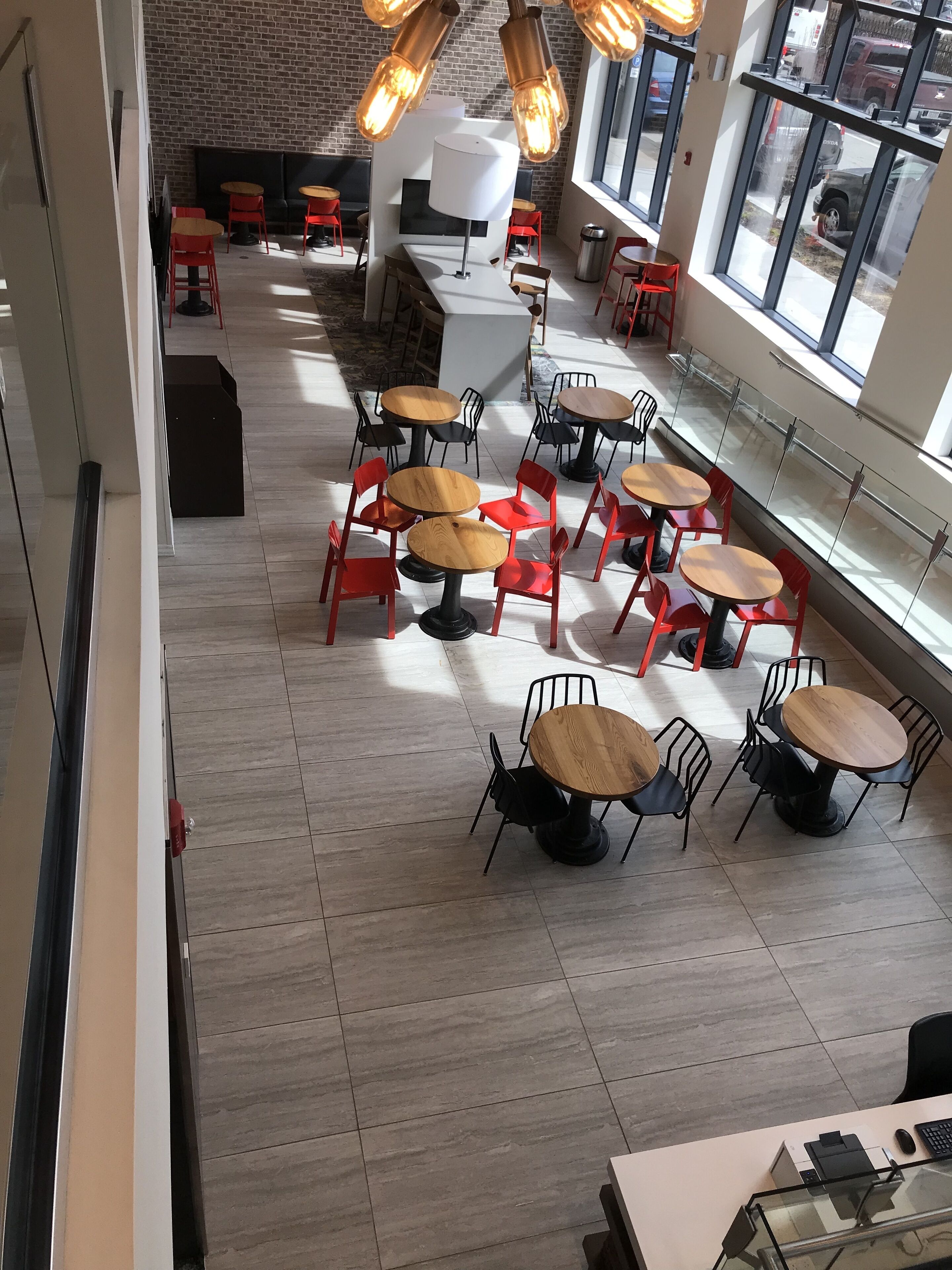 A modern cafe with round tables and red chairs, a brick wall, and large windows.