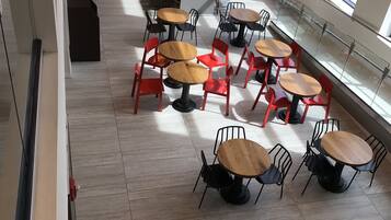 Un caffè moderno con tavoli rotondi e sedie rosse, una parete in mattoni e ampie finestre.