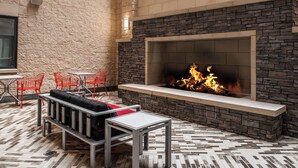 An outdoor seating area with a stone fireplace, red chairs, and a metal table. - Residence Inn Pittsburgh Oakland/University Place (Pittsburgh)