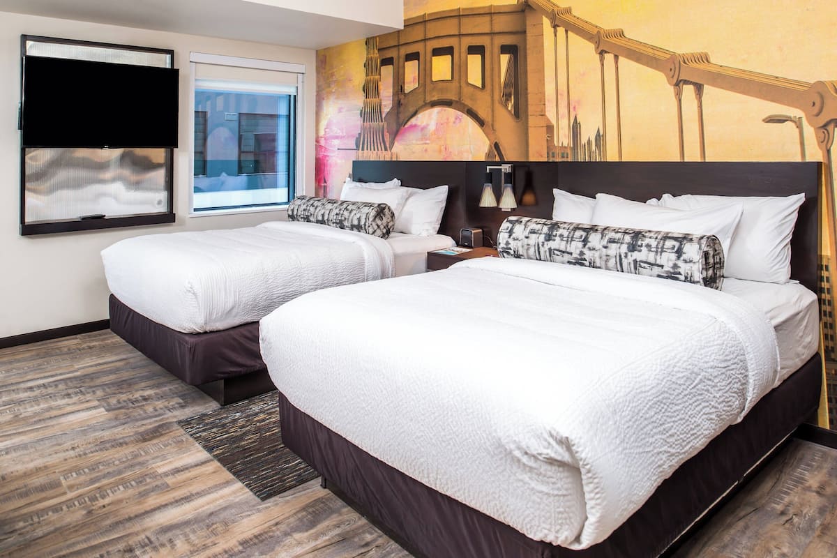 A hotel room with two beds, a large window, a wall mural, and a flat-screen TV.