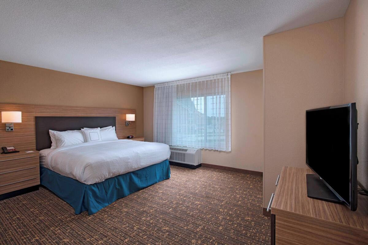 Ein Hotelzimmer mit einem Bett, einem Fernseher, einem Schreibtisch und einem Vorhangfenster.