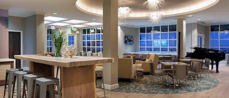 A spacious lobby with a central bar area, comfortable seating, and a grand piano.