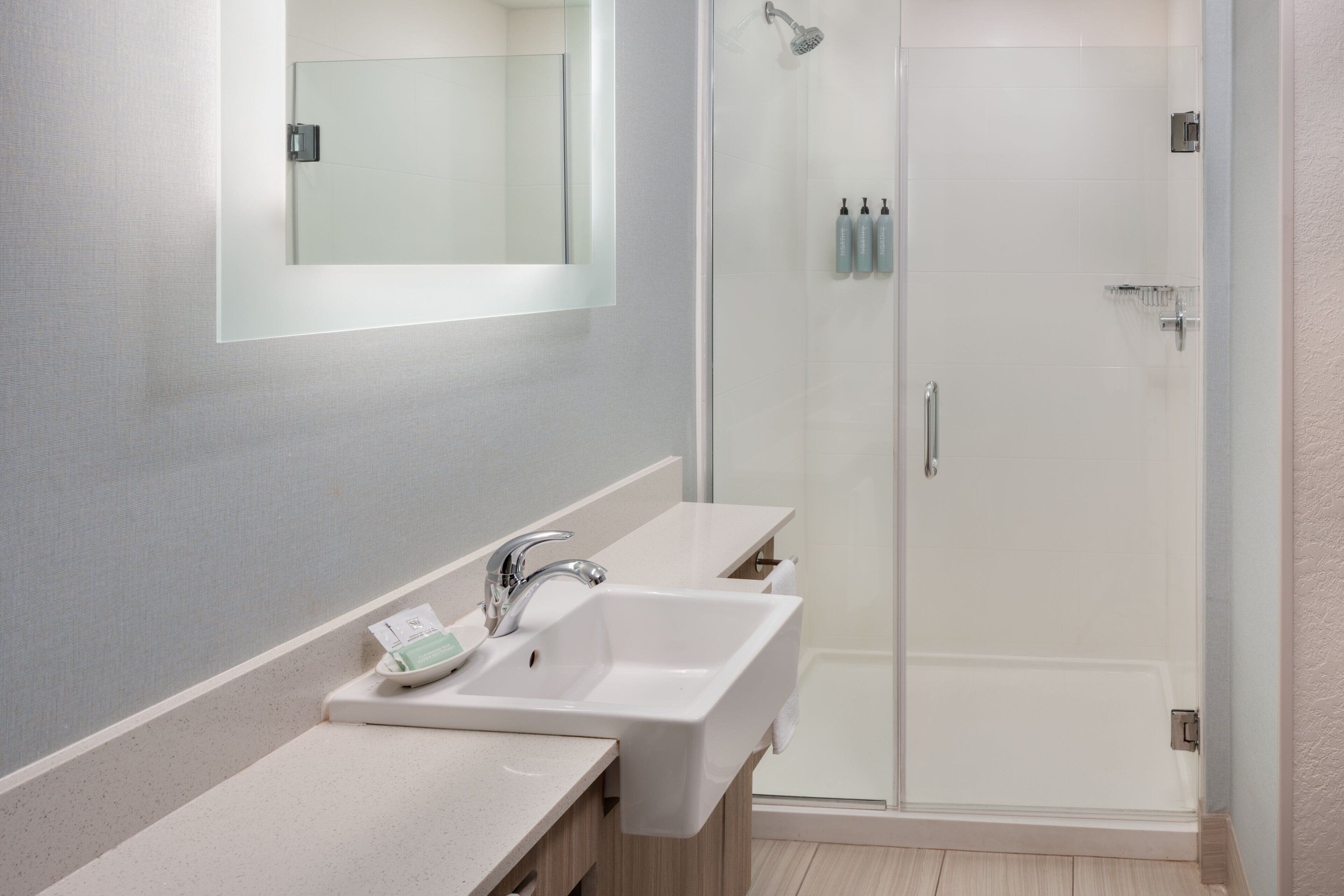 A modern bathroom with two sinks, a mirror, and a glass-enclosed shower.
