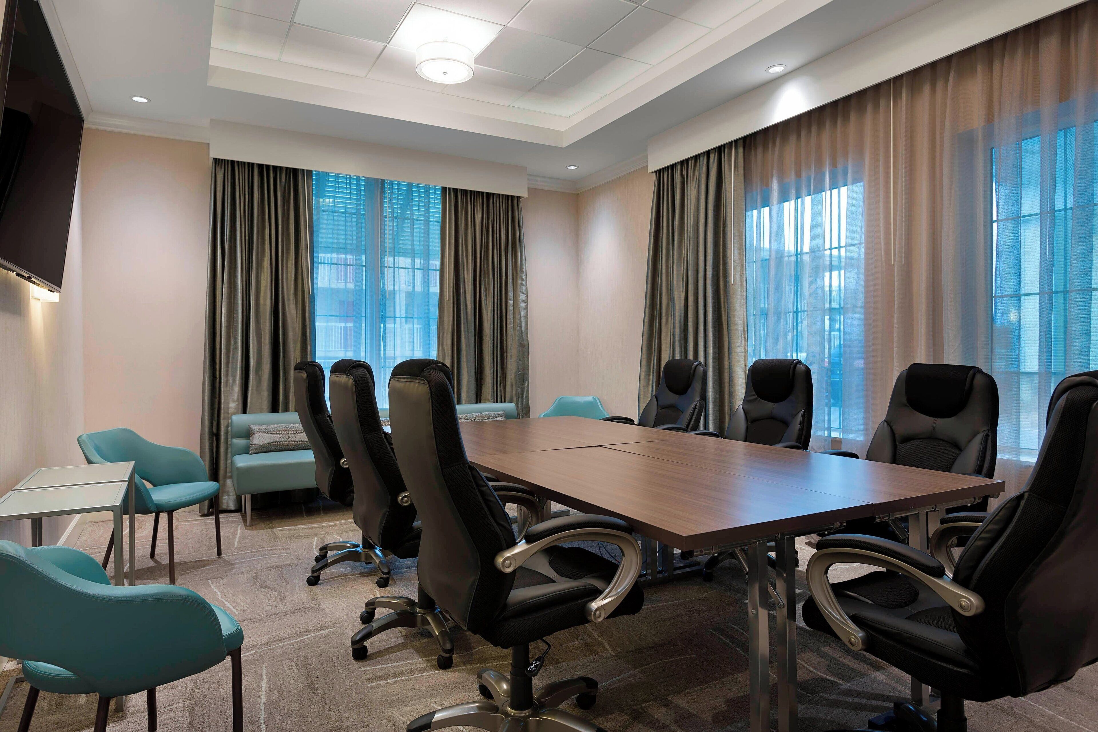 Een vergaderruimte met een grote tafel, zwarte bureaustoelen, blauwgroene fauteuils en een bank.
