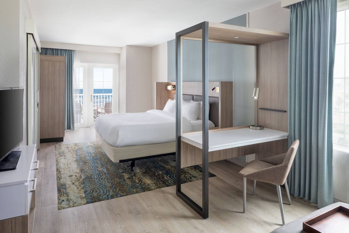 Una camera d'albergo con un letto, una scrivania, una sedia, una TV e vista sul mare.