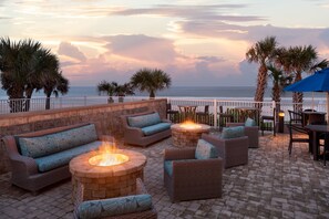 Eine Terrasse mit Korbmöbeln, Feuerstellen und Blick auf das Meer bei Sonnenuntergang.