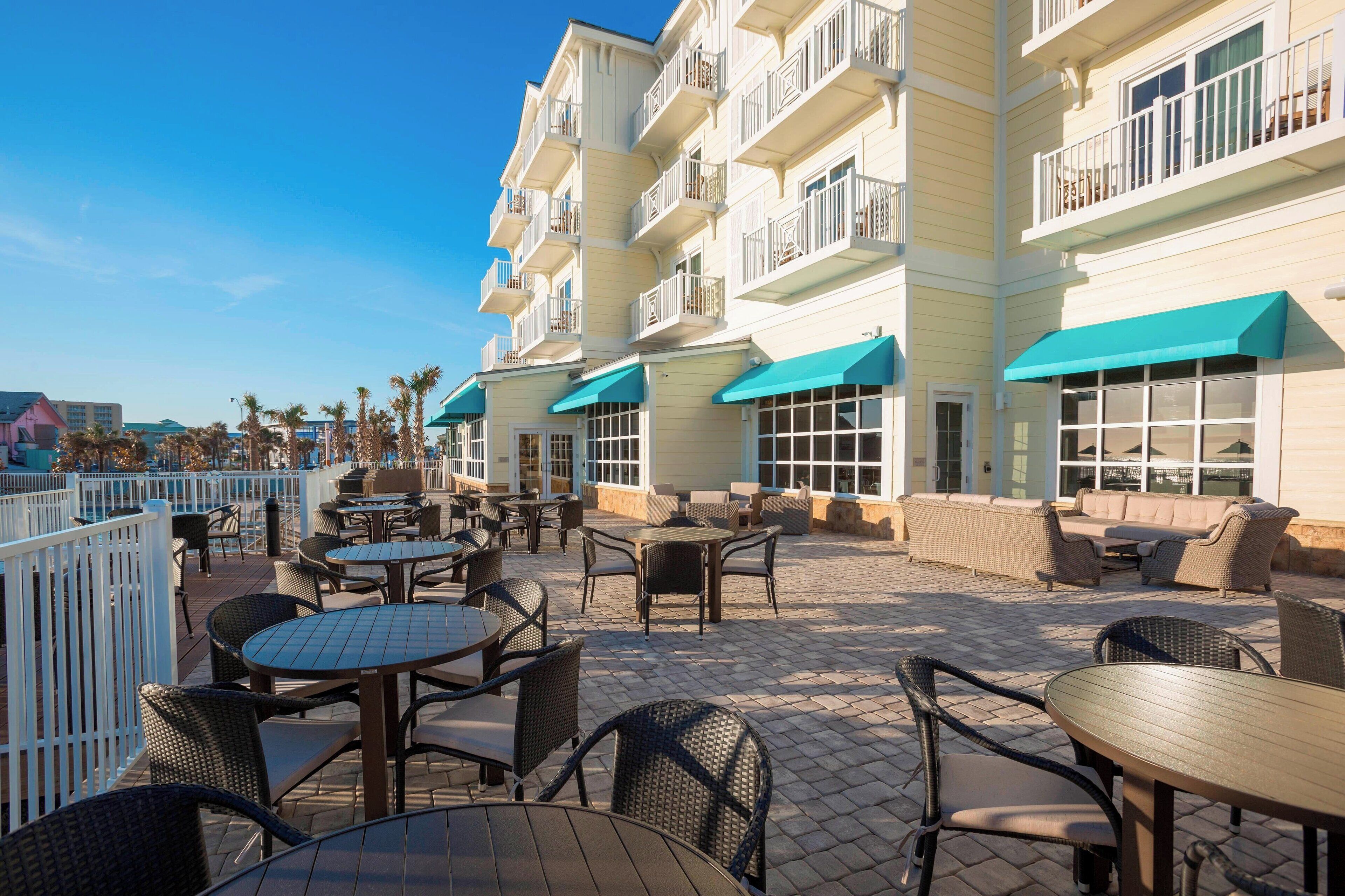 An outdoor patio area with tables and chairs, a pool, and a building with balconies.