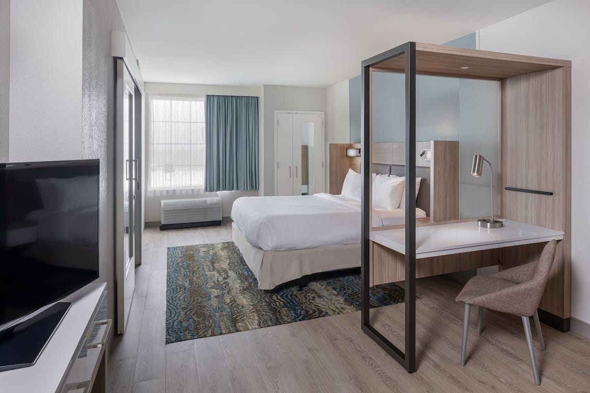 Camera d'albergo moderna con un letto, una scrivania, una sedia, una TV e un'ampia finestra con tende.