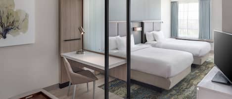 Une chambre d’hôtel avec un bureau, deux lits, une télévision et un tableau au mur.