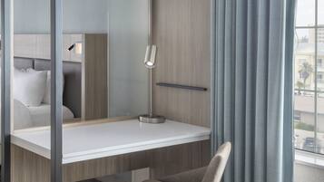Quarto moderno com cama de solte e escrivaninha, uma cadeira, luminária e vista para o exterior.