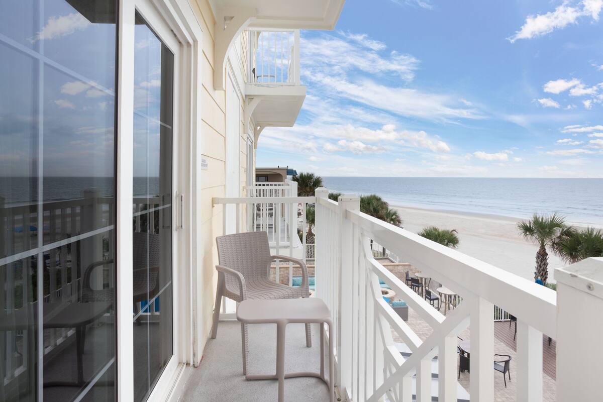Un balcone con vista sulla spiaggia, una sedia e un tavolo.