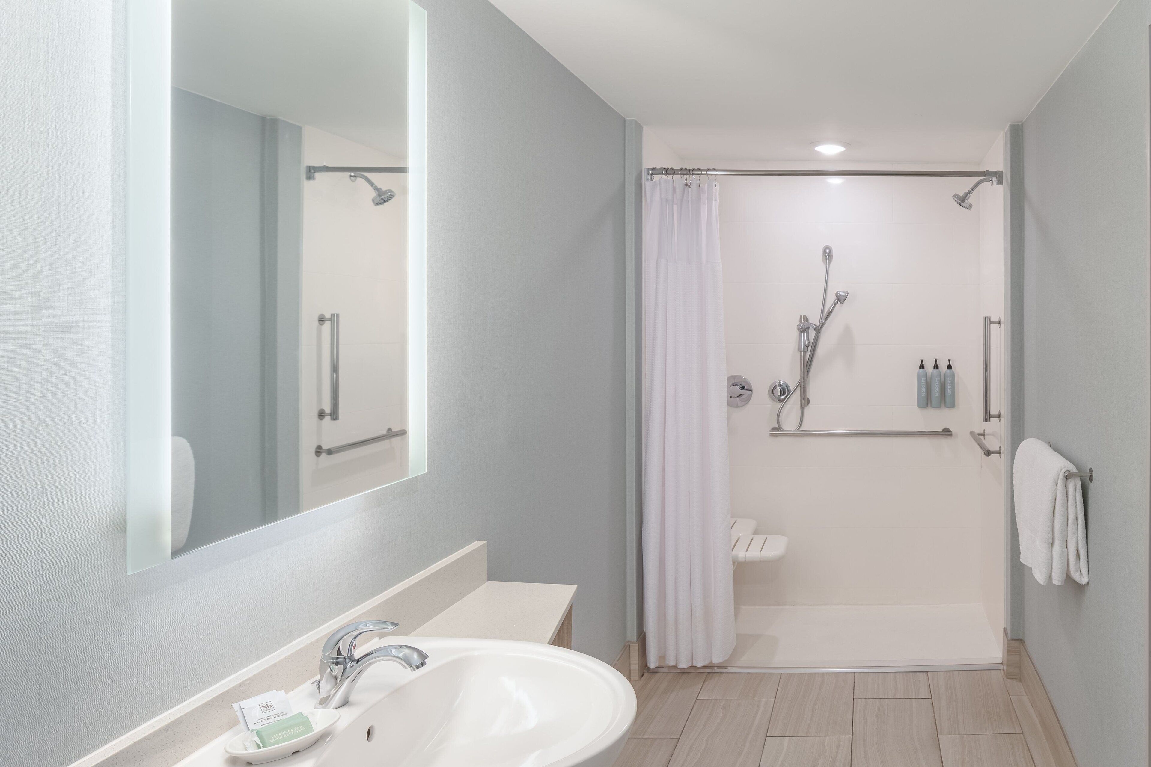 Een moderne badkamer met een wastafel, spiegel, douche en toilet.