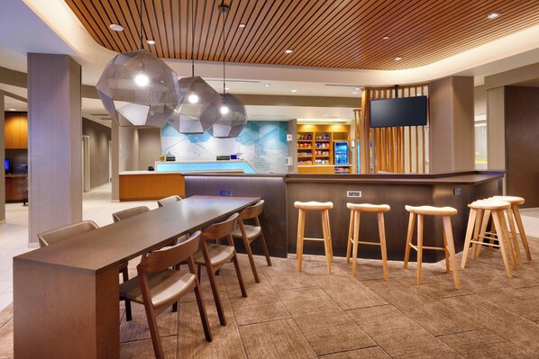 Un hall d’hôtel moderne avec un comptoir d’accueil en bois, un bar et des espaces pour s’asseoir.
