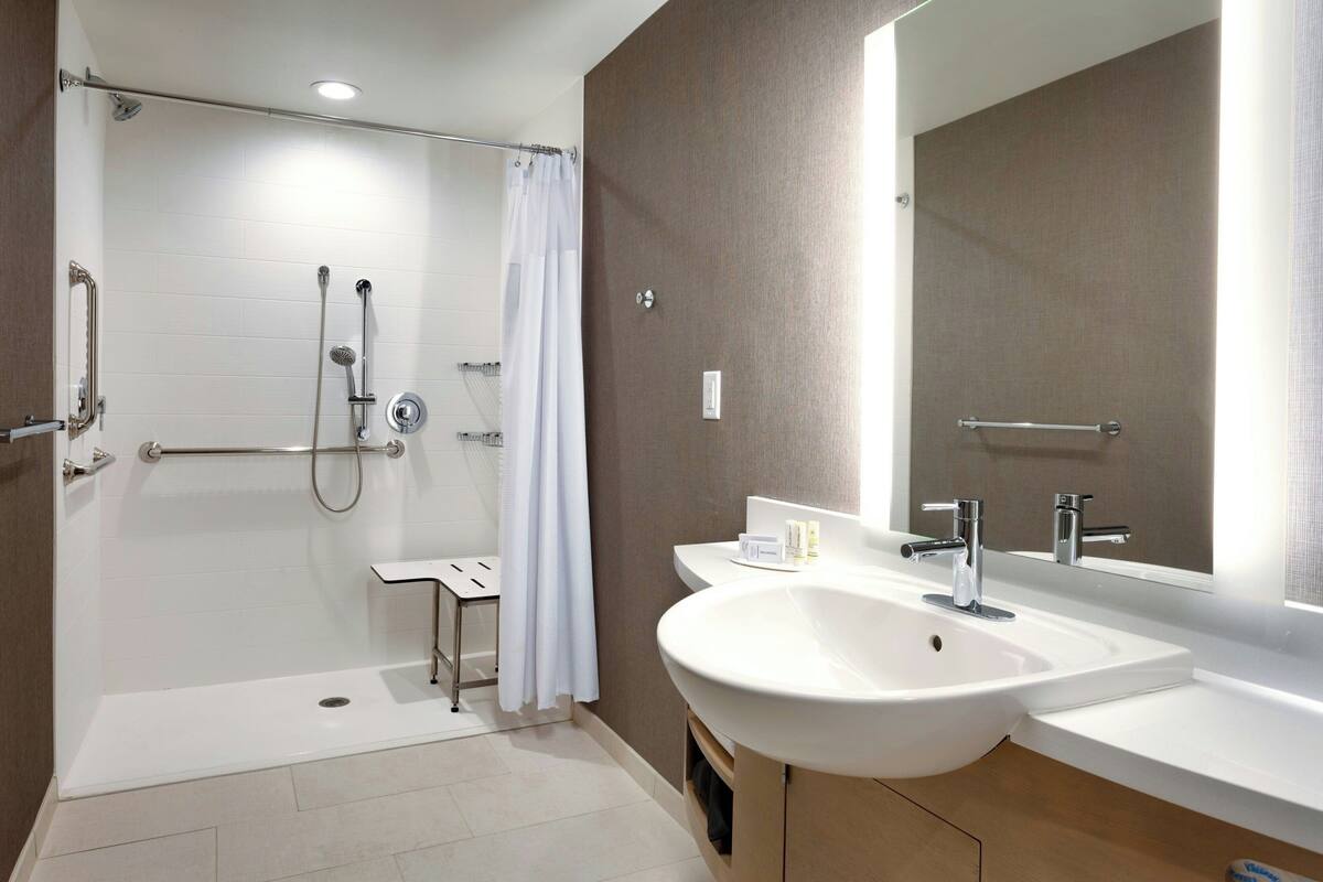 Ein modernes Badezimmer mit barrierefreier Dusche, einem großen Waschbecken und einem Spiegel.
