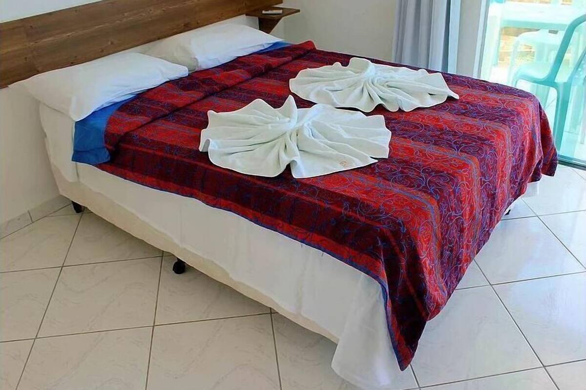 A neatly made bed with a red and blue patterned bedspread, white pillows, and two white towels arranged on the bed.