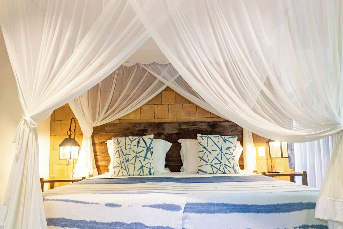 A bed with a canopy, a stone wall, and two bedside lamps.