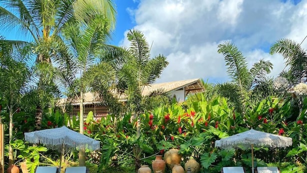 A poolside area with lounge chairs and umbrellas, surrounded by lush greenery and tropical plants. - Hotel Boutique Casa de Perainda (Porto Seguro)