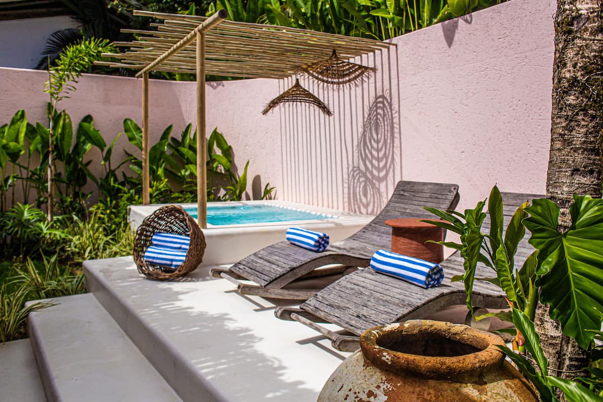 A poolside area with lounge chairs, a hot tub, and a pergola with hanging lights.