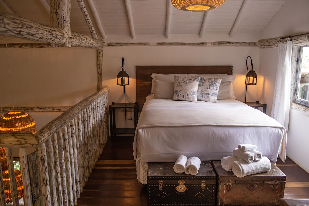 A bedroom with a wooden headboard, a bed with white linens, two bedside lamps, and a window with curtains.