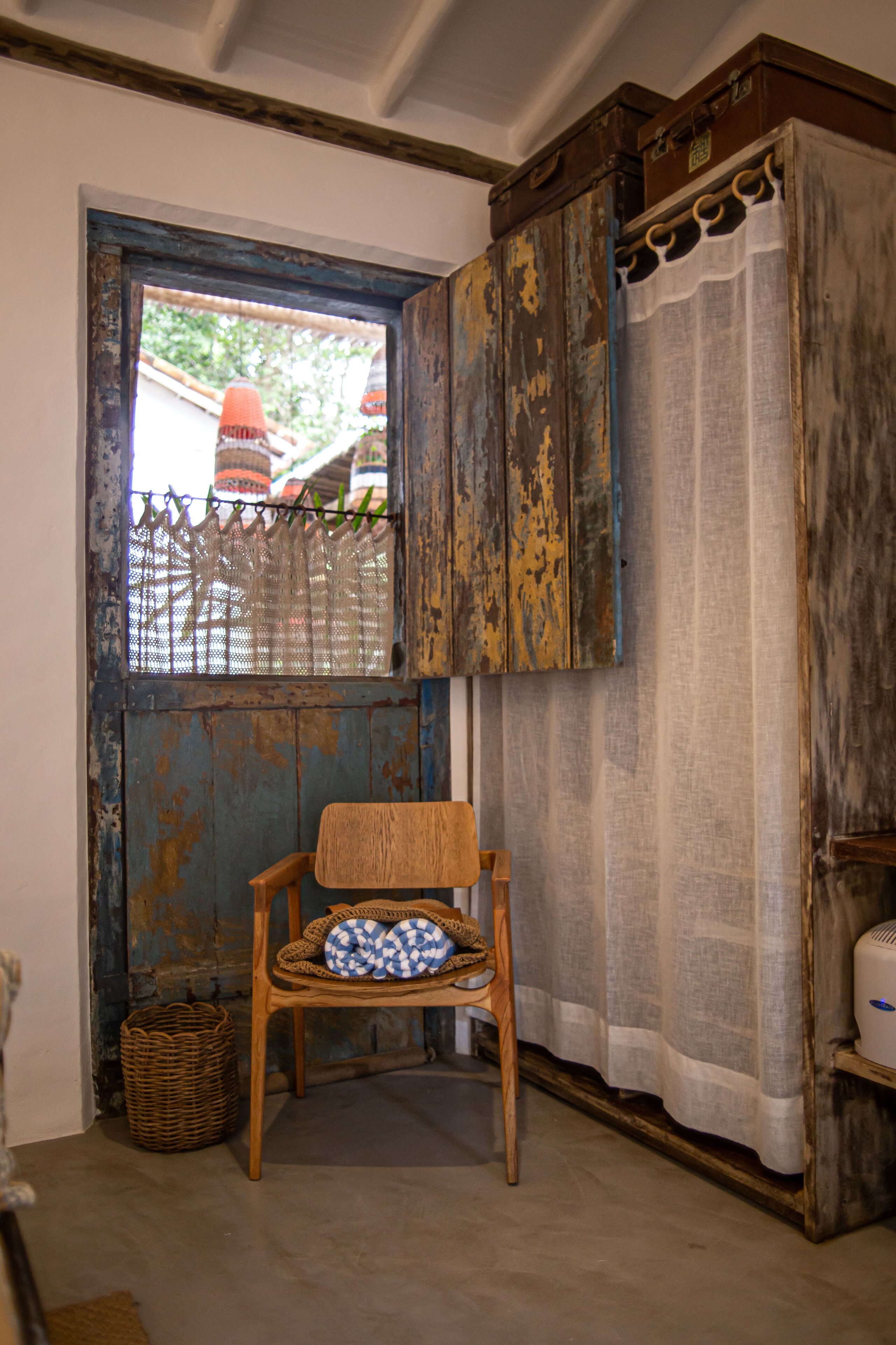 A rustic room with a wooden chair, a wicker basket, and a window with a curtain.