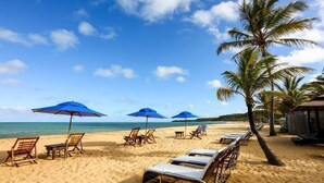 A beach with sun loungers, umbrellas, and a palm tree. - Hotel Boutique Casa de Perainda (Porto Seguro)