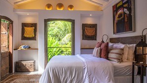 A bedroom with a large bed, a window with a view of greenery, a wooden chest, and a painting on the wall. - Hotel Boutique Casa de Perainda (Porto Seguro)