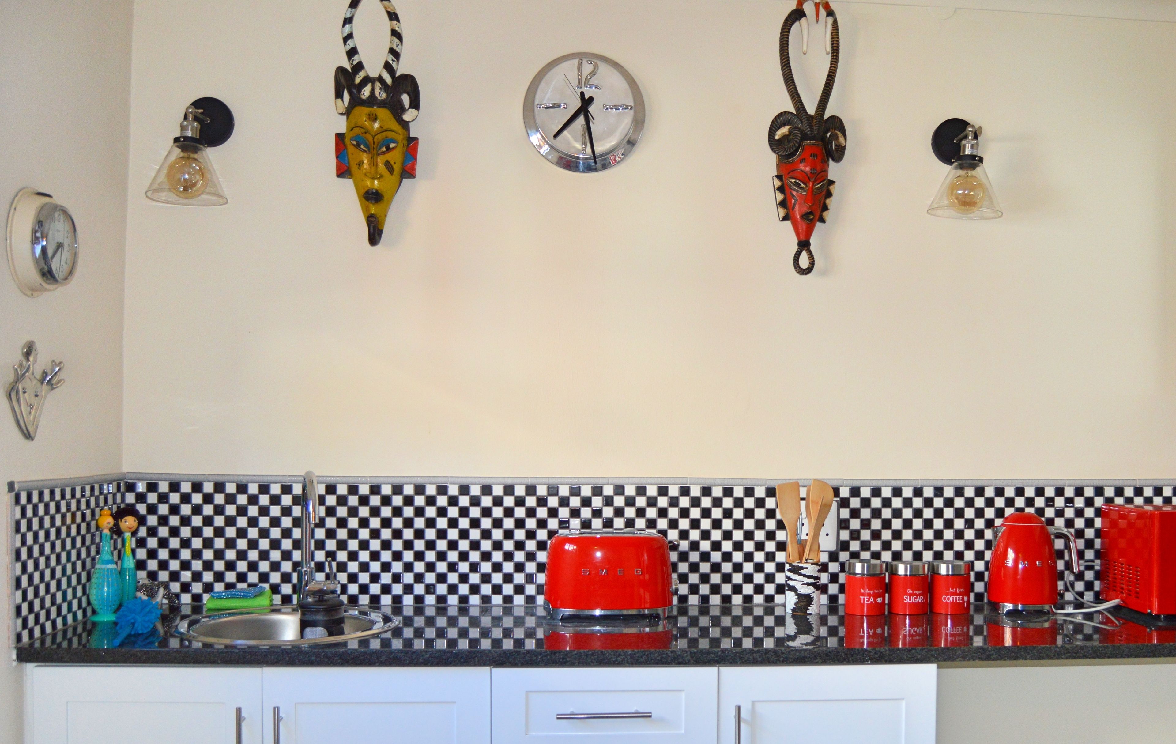 A kitchen with a checkered backsplash, a red toaster, and various kitchen utensils.