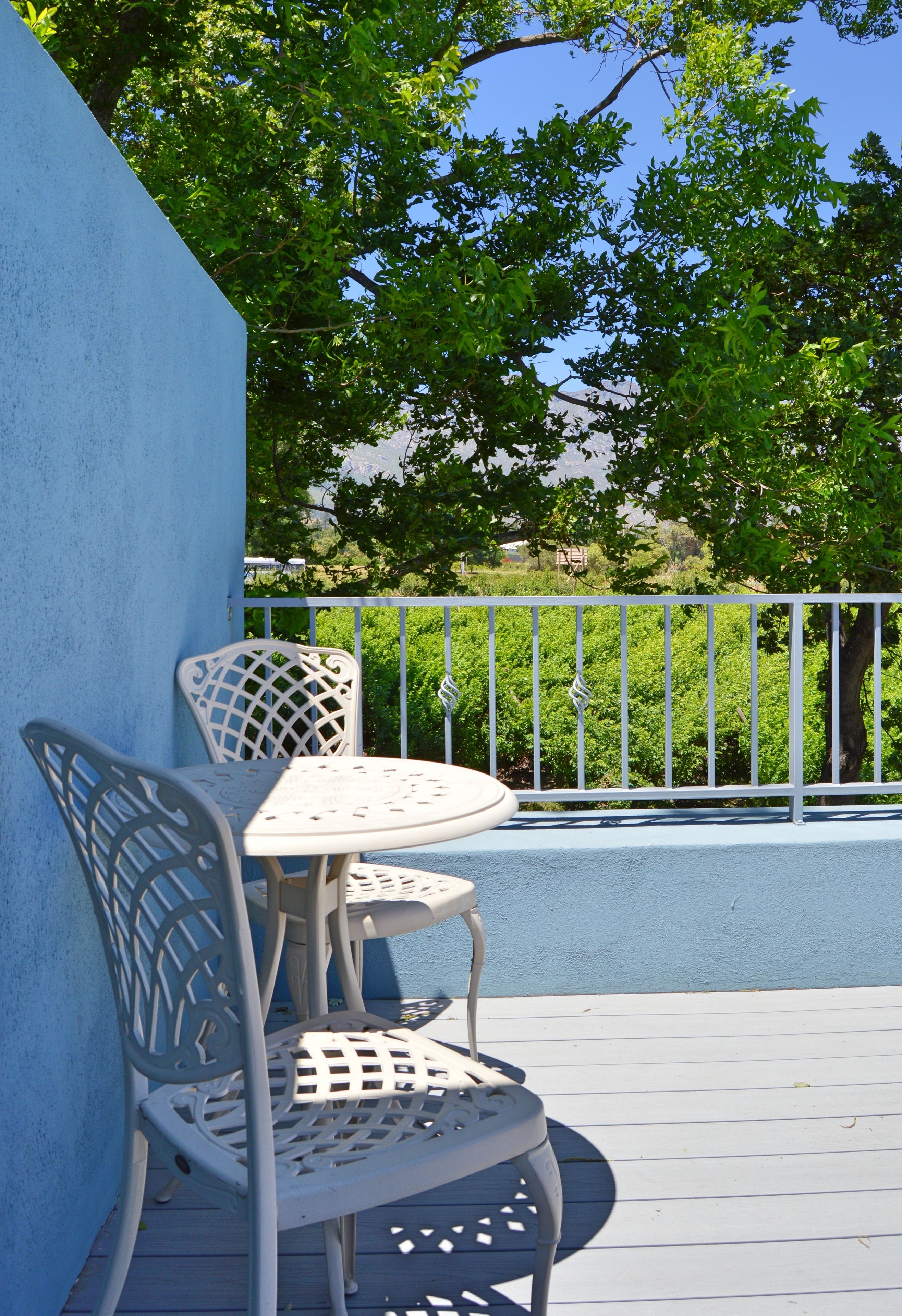 A balcony with a white metal table and chairs, a blue wall, and a white metal railing.