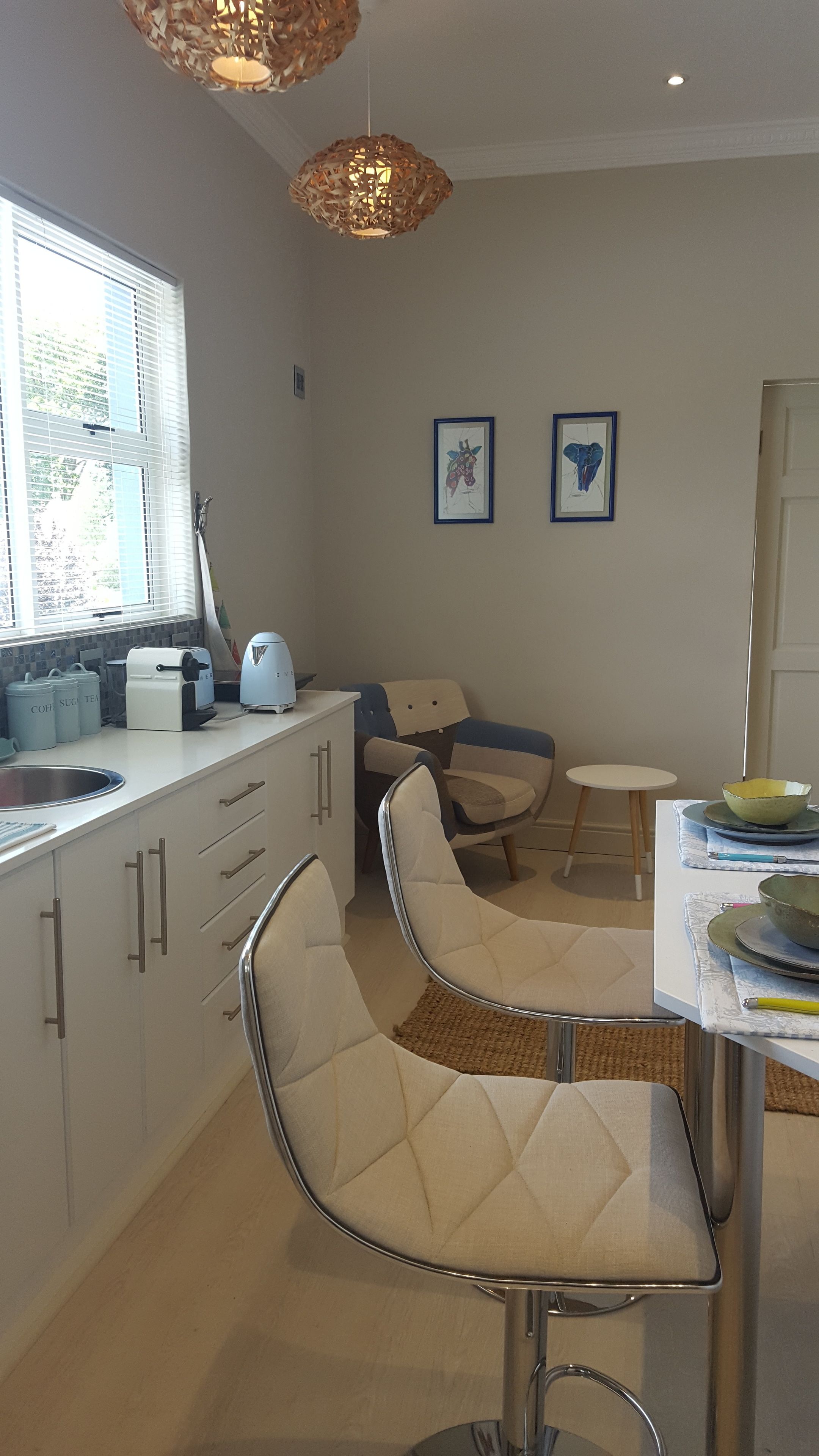 Una cocina moderna con armarios blancos, una cafetera y un comedor con una mesa redonda y dos sillas.