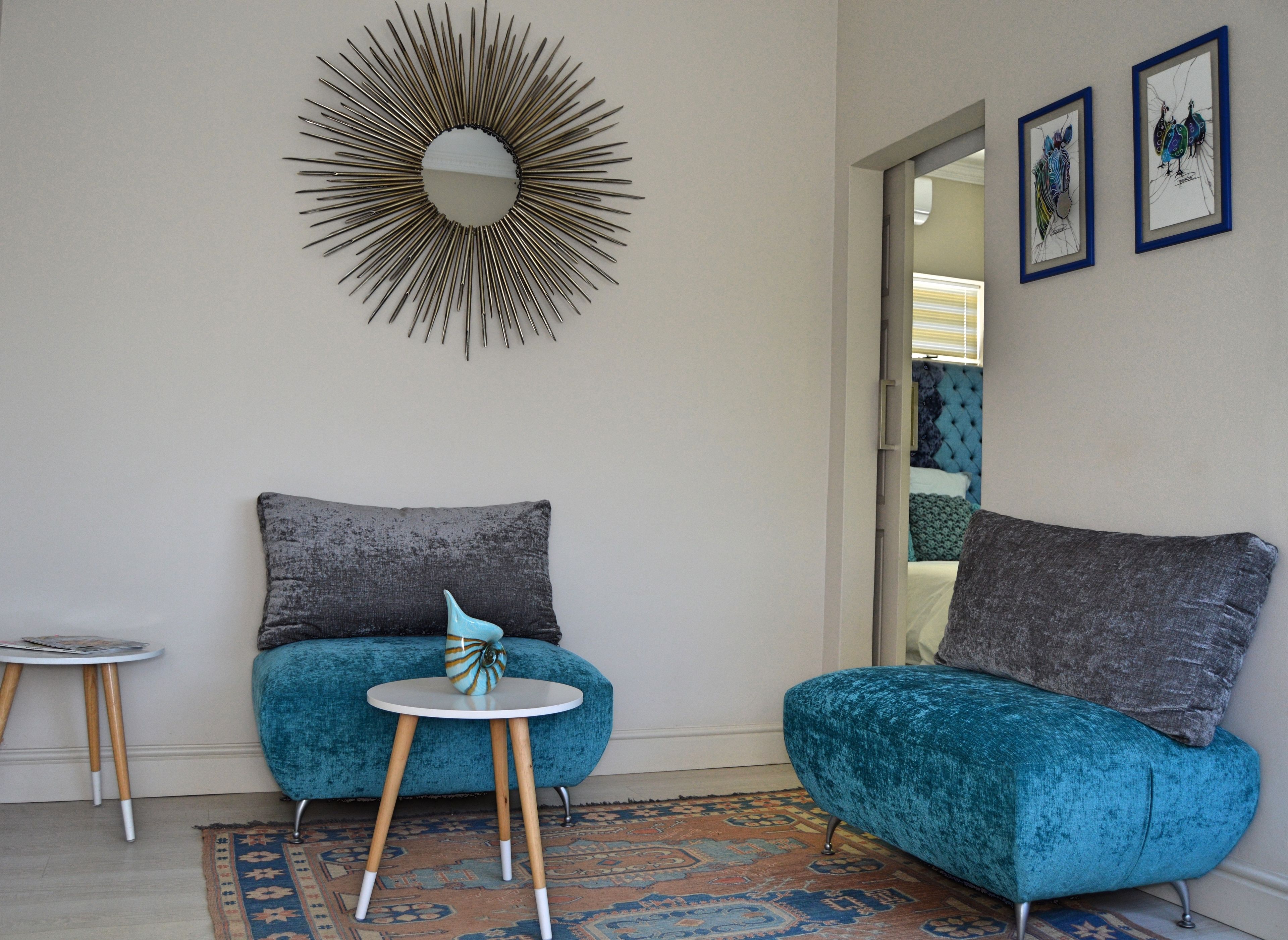 Une pièce comprenant un canapé en velours turquoise, une petite table ronde surmontée d’un vase bleu et blanc, un miroir décoratif et un tapis à motifs.
