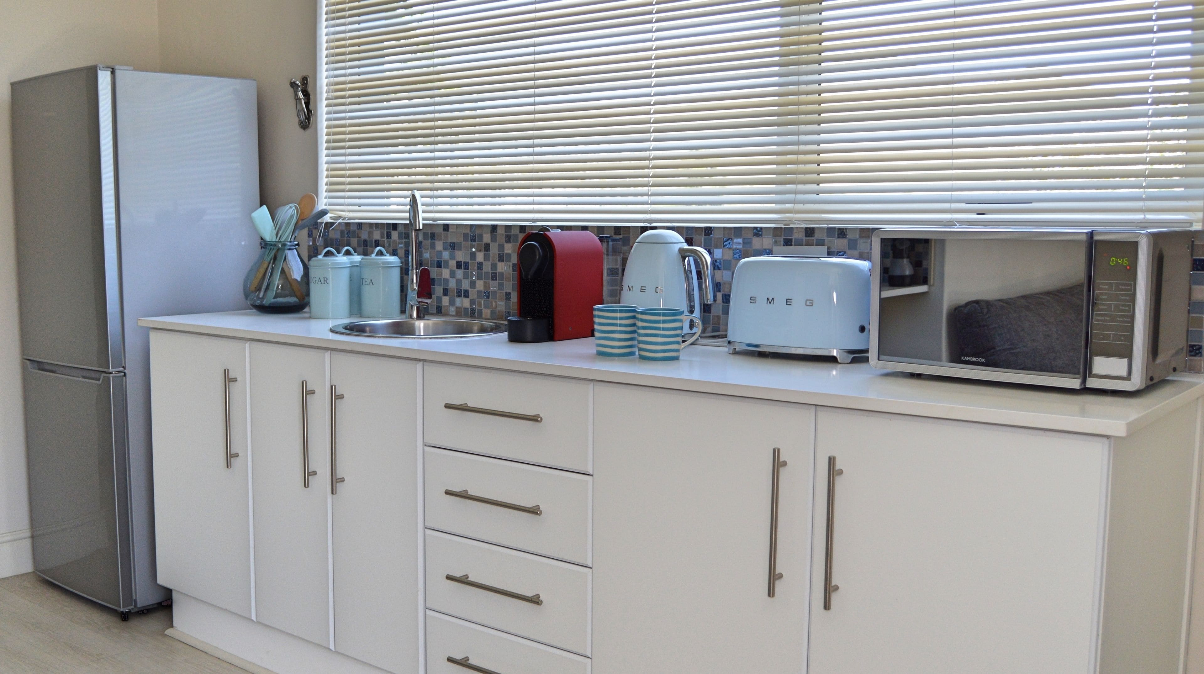 A modern kitchen with a built-in refrigerator, a toaster, a kettle, and a microwave.