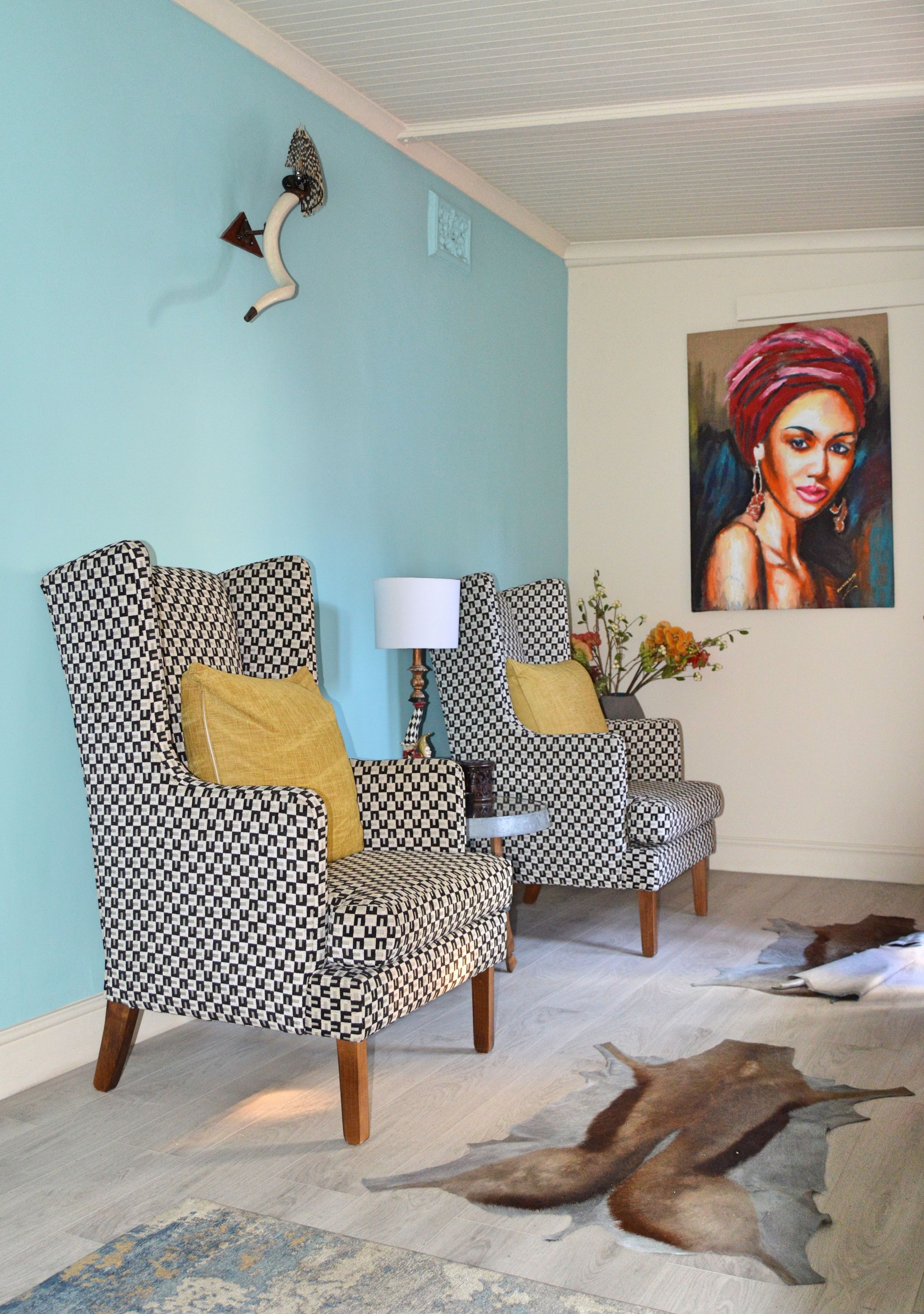 Een kamer met twee gestreepte fauteuils, een lamp, een schilderij en een bont kleed.