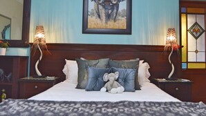 A bedroom with a large bed, two bedside lamps, a framed elephant painting, and a nightstand with a lamp. - 1AA Wilhelminia Apartments (Franschhoek)