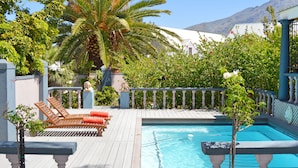 A pool area with wooden deck, lounge chairs, and a palm tree. - 1AA Wilhelminia Apartments (Franschhoek)